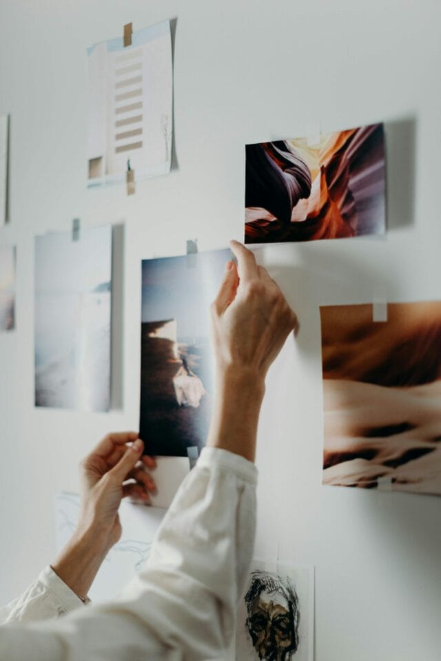 A person in a white shirt is navigating the arrangement of stock photos on a white wall, focusing on landscapes and abstract art. One hand adjusts an image depicting a vivid canyon scene, mastering the dos and don'ts of a perfect display